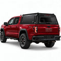 A red GMC Canyon pickup truck shown from a rear three-quarter angle, fitted with a black Gullwing Caps aerowing truck canopy, set against a plain white studio background.