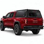 A red GMC Canyon pickup truck shown from a rear three-quarter angle, fitted with a black Gullwing Caps aerowing truck canopy, set against a plain white studio background.