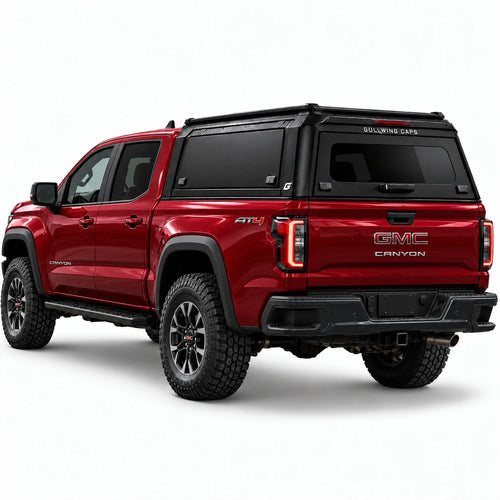 A red GMC Canyon pickup truck shown from a rear three-quarter angle, fitted with a black Gullwing Caps aerowing truck canopy, set against a plain white studio background.