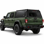 An olive green Jeep Gladiator pickup truck shown from a rear three-quarter angle, fitted with a black Gullwing Caps aerowing truck canopy, set against a plain white studio background.
