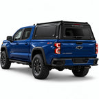 A blue Chevrolet Colorado pickup truck shown from a rear three-quarter angle, fitted with a black Gullwing Caps aerowing truck canopy, set against a plain white studio background.