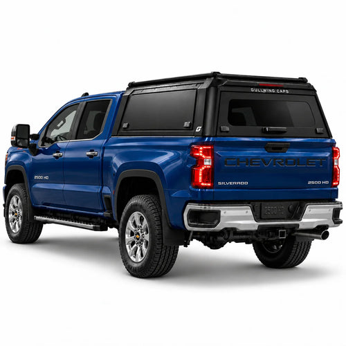 A blue Chevrolet Silverado 2500 HD pickup truck shown from a rear three-quarter angle, fitted with a black Gullwing Caps aerowing truck canopy, set against a plain white studio background.