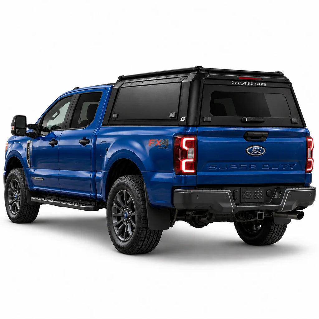 A blue Ford f250 Super Duty FX4 pickup truck shown from a rear three-quarter angle, fitted with a black Gullwing Caps aerowing truck canopy, set against a plain white studio background.