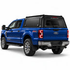 A blue Ford f350 Super Duty pickup truck shown from a rear three-quarter angle, fitted with a black Gullwing Caps aerowing truck canopy, set against a plain white studio background.