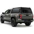 A gray Toyota Tacoma pickup truck shown from a rear three-quarter angle, fitted with a black Gullwing Caps aerowing truck canopy, set against a plain white studio background.