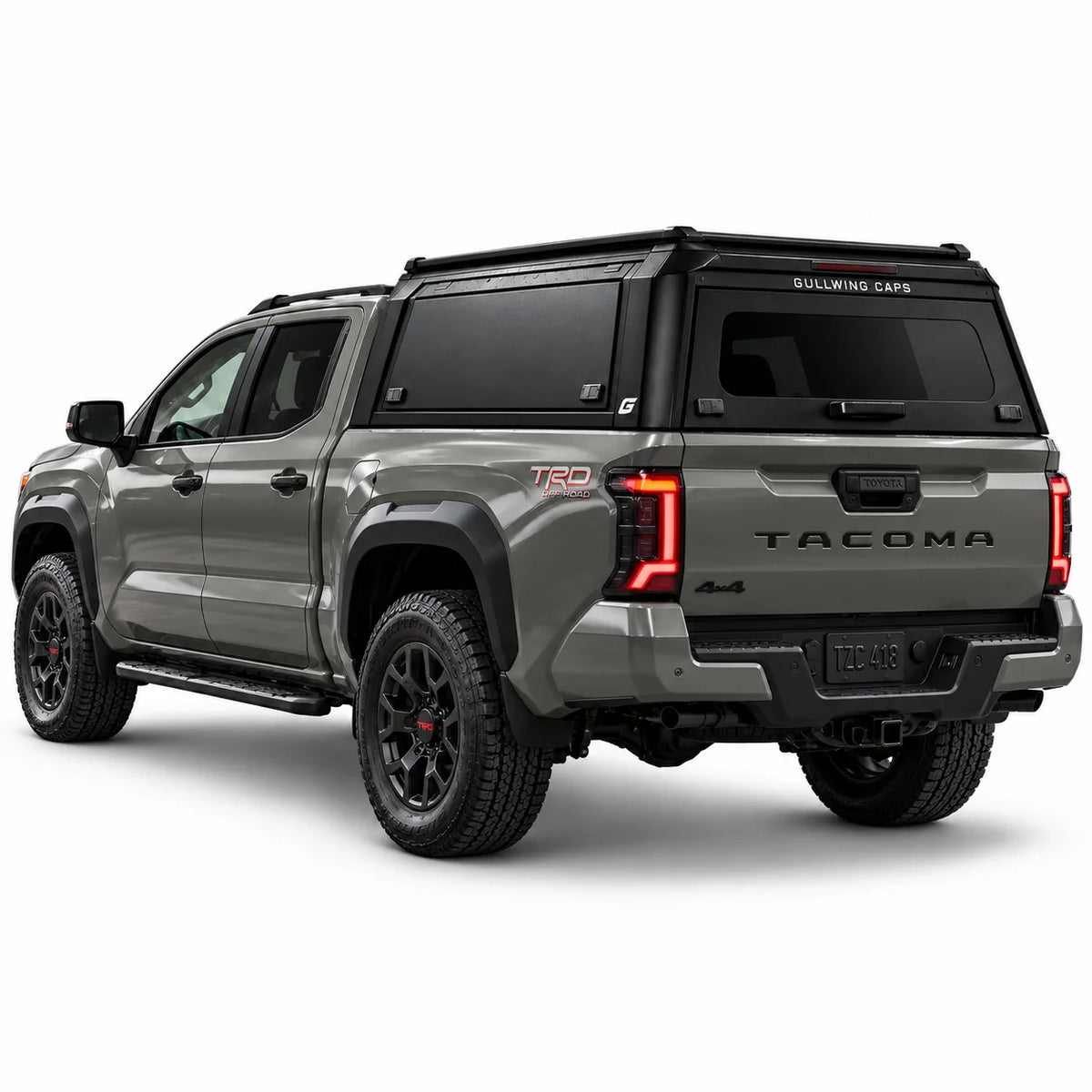 A gray Toyota Tacoma pickup truck shown from a rear three-quarter angle, fitted with a black Gullwing Caps aerowing truck canopy, set against a plain white studio background.