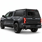 A dark gray Tundra 4x4 pickup truck shown from a rear three-quarter angle, fitted with a black Gullwing Caps aerowing truck canopy. The truck features black wheels, black side steps, and red accents on the TRD badge and wheel centers, set against a plain white studio background.